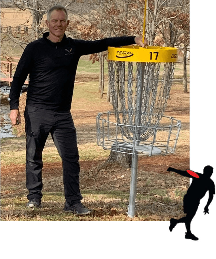Lavone Wolfe stands beside a disc golf basket marked with the number 17 in an outdoor park setting